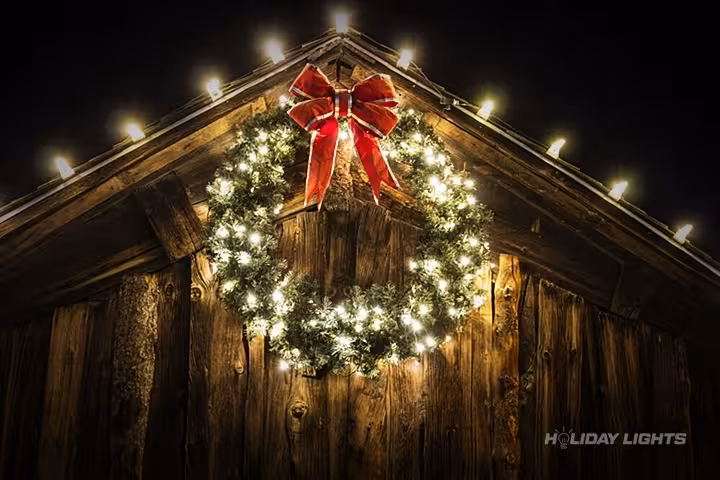 Barn Christmas lights installation with warm white roofline lighting and festive wreath decoration in Massachusetts